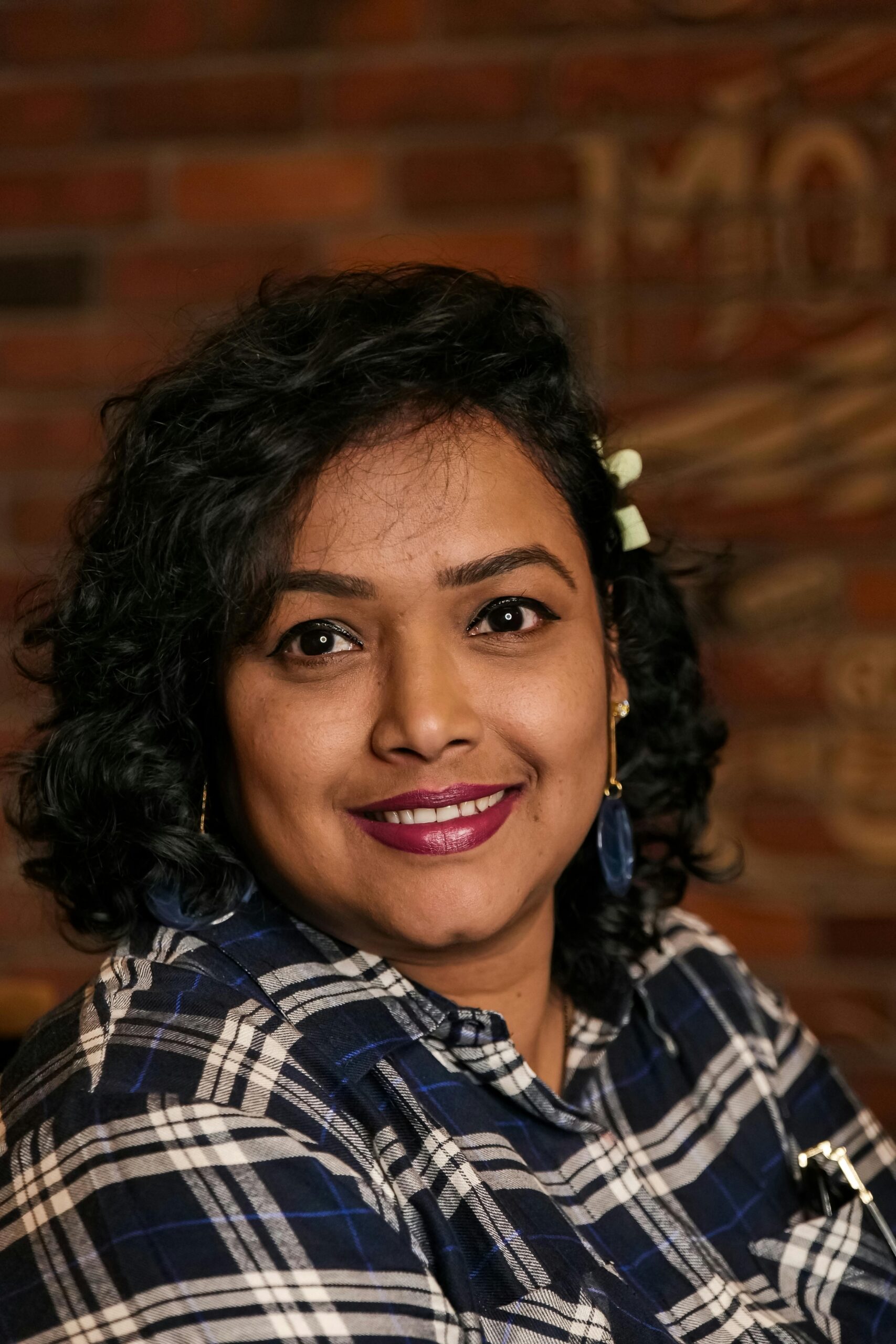 Charming portrait of a woman with curly hair and a plaid shirt against a brick wall.